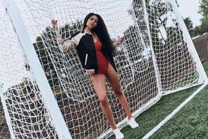fotboll flicka. full längd av attraktiv ung kvinna i sport Kläder ser på kamera medan stående nära de mål posta foto