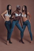 så varm full längd av tre attraktiv ung kvinnor Framställ medan stående mot brun bakgrund foto