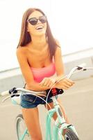njuter en sorglös dag utomhus. skön ung kvinna lutande på henne cykel och leende foto