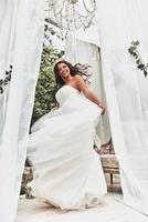 dans brud. full längd av attraktiv ung kvinna i bröllop klänning leende och ser på kamera medan spinning runt om utomhus foto