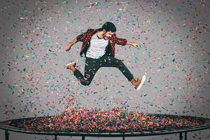 levande en ljus liv. i luften skott av stilig ung man Hoppar på trampolin med konfetti Allt runt om honom foto