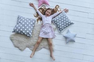 tycka om en stjärna. topp se av söt liten flicka förvaring ögon stängd och leende medan liggande på de golv bland kuddar foto