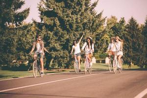 utgifterna bra tid med vänner. grupp av ung människor ridning cyklar längs en väg och ser Lycklig foto