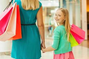 liten shopaholic. bak- se av mor och dotter innehav handla påsar medan liten flicka ser över axel och leende foto