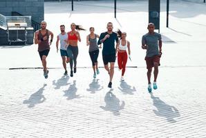full längd topp se av människor i sporter Kläder joggning medan utövar på de trottoar utomhus foto