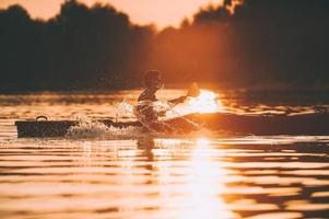 möte solnedgång på kajak. sida se av man Kajakpaddling på flod med solnedgång i de bakgrund foto