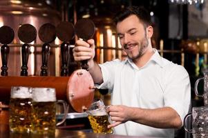 nyligen knackade öl. glad ung bartender häller öl och leende foto