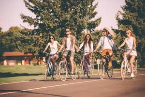 perfekt dag för cykling. grupp av ung människor ridning cyklar längs en väg och ser Lycklig foto