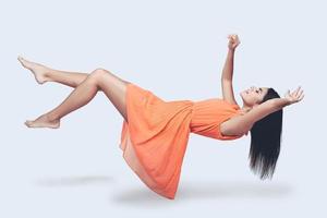 flygande så hög. full längd studio skott av attraktiv ung kvinna i orange klänning svävande i luft och förvaring ögon stängd foto
