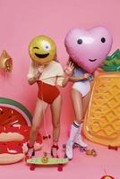 låta de fest satte igång full längd av två ung kvinnor i badkläder beläggning ansikten med ballonger medan stående mot rosa bakgrund foto