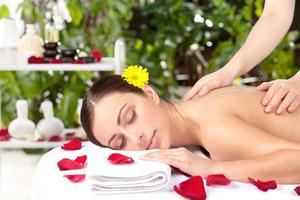 spa flicka. skön ung kvinna med blomma i huvud liggande på främre medan massage terapeut masse henne tillbaka foto