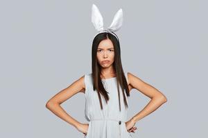 uttråkad kanin. arg ung asiatisk kvinna i kanin öron ser på kamera medan stående mot grå bakgrund foto