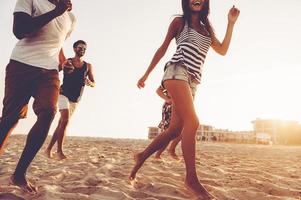 sorglös springa. grupp av ung glad människor löpning längs de strand och ser Lycklig foto