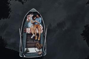 kärleksfull par i båt. topp se av skön ung par fattande och leende medan liggande i de båt foto