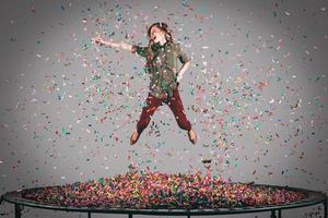 roligt i rörelse. i luften skott av skön ung kvinna Hoppar på trampolin med konfetti Allt runt om henne foto