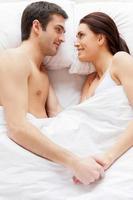 kärleksfull par i säng. topp se av skön ung kärleksfull par liggande i säng och innehav händer foto