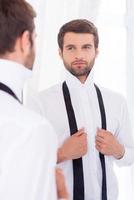 framställning till en särskild dag. stilig ung man i vit skjorta och obundet slips stående mot spegel foto