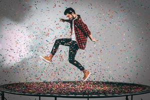 trampolin roligt. i luften skott av stilig ung man Hoppar på trampolin med konfetti Allt runt om honom foto