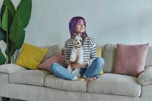 glad Tonårs flicka bärande liten hund medan avkopplande på de soffa på Hem foto
