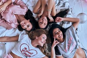 verklig roligt. topp se av fyra lekfull ung kvinnor leende medan liggande på de säng på Hem foto