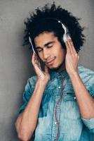 flytande bort med musik. ung afrikansk man justeras hörlurar och förvaring ögon stängd medan stående mot grå bakgrund foto