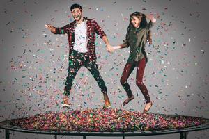 bara för roligt. i luften skott av skön ung glad par innehav händer medan Hoppar på trampolin tillsammans med konfetti Allt runt om dem foto