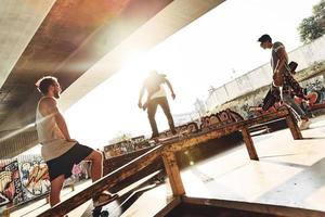 praktiserande deras knep. grupp av ung människor skateboard medan hängande ut på de skridsko parkera utomhus foto