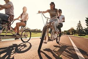 känner tycka om flygande. grupp av Lycklig ung människor i tillfällig ha på sig leende medan cykling tillsammans utomhus foto