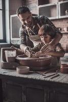 krukarbete med far. glad ung man och liten pojke framställning keramisk pott på de krukmakeri klass foto