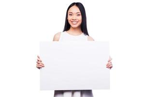 reklam din produkt. skön ung asiatisk kvinna innehav kopia Plats och leende medan stående mot vit bakgrund foto