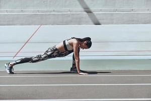 håller på med henne bäst. skön ung kvinna i sporter Kläder utövar medan stretching på de löpning Spår utomhus foto