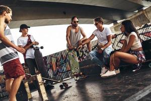 bara hängande med vänner. grupp av ung modern människor talande medan utgifterna tid på de skateboard parkera utomhus foto