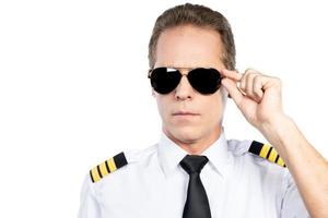 självsäker pilot. självsäker manlig pilot i enhetlig justeras hans glasögon medan stående mot vit bakgrund foto