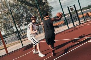 bra spel. två ung män i sporter Kläder spelar basketboll medan utgifterna tid utomhus foto