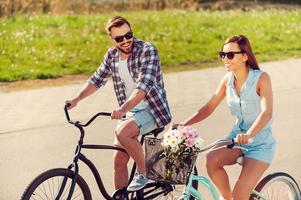 njuter de sommar cykel rida. glad ung par ridning på cyklar längs de väg foto
