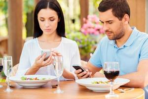 par från digital ålder. ung par skriver något på deras smart telefoner medan avkopplande i utomhus restaurang tillsammans foto