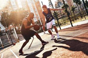 som visar hans Kompetens. två ung män i sporter Kläder spelar basketboll medan utgifterna tid utomhus foto