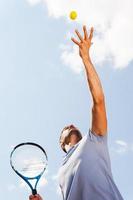 tjänande en boll. låg vinkel se av tennis spelare tjänande en boll medan stående mot blå himmel foto