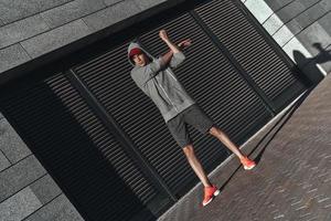 stretching övningar. full längd av ung man i sporter Kläder uppvärmningen upp medan utövar utanför foto