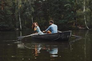 Nej bryr sig. skön ung par njuter romantisk datum och leende medan rodd en båt foto