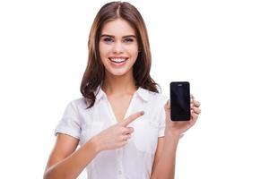 du Maj ser du annons här. skön ung kvinnor innehav mobil telefon och pekande på den medan stående mot vit bakgrund foto