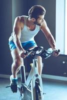 rida till Framgång. ung stilig man i sportkläder cykling på Gym foto