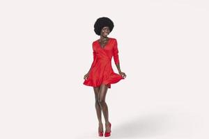 full längd av skön ung afrikansk kvinna i röd klänning dans mot bakgrund foto