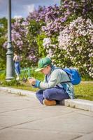 en ung man är Sammanträde på de sida av en lila gränd och ser på hans telefon. mot de bakgrund av lila buskar. interaktioner. selektiv fokus. foto