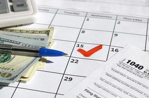1040 enskild inkomst beskatta lämna tillbaka tom med dollar räkningar, kalkylator och penna på kalender sida med markant 15:e april foto