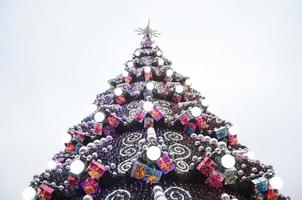 en fragment av en enorm jul träd med många ornament, gåva lådor och lysande lampor. Foto av en dekorerad jul träd närbild med kopia Plats