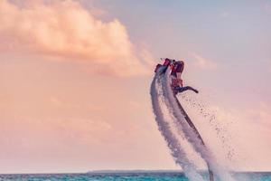 maldiverna ö solnedgång. professionell flyga styrelse ryttare håller på med tillbaka flip med tropisk tillflykt ö bakgrund. solnedgång sport och sommar aktivitet bakgrund, roligt vatten sport foto