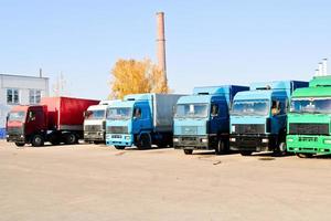 stor tung frakt lastbilar med hytter och trailers stå i en rad redo för leverans av frakt på de industriell raffinaderi mot de bakgrund av rör, transport logistik affär foto