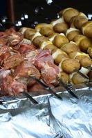 rå kött och potatisar är planterade på metall spett. de bearbeta av matlagning shish kebab. ryska och ukrainska läger mat foto