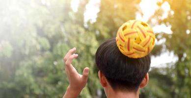 ung sydöst asiatisk manlig sepak takraw spelare använder sig av hans rätt hand till håll boll på hans huvud, utomhus- sepak takraw spelar efter skola, mjuk och selektiv fokus på boll. foto